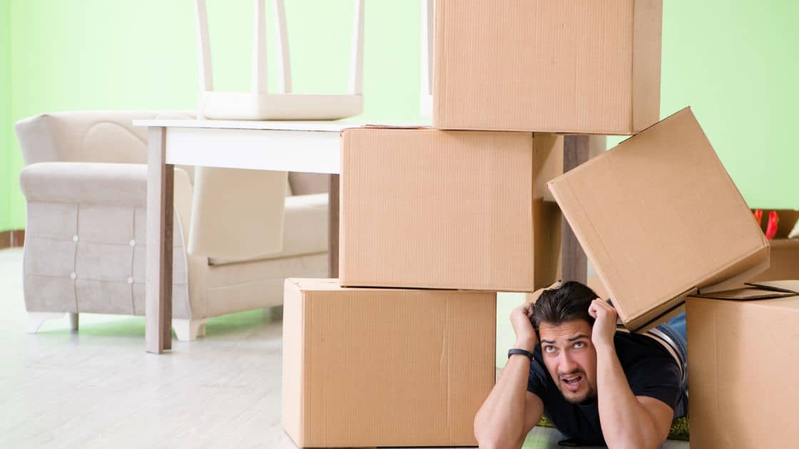 A man in distress amongst moving boxes: It is crucial to plan your move wisely, as it can be expensive.